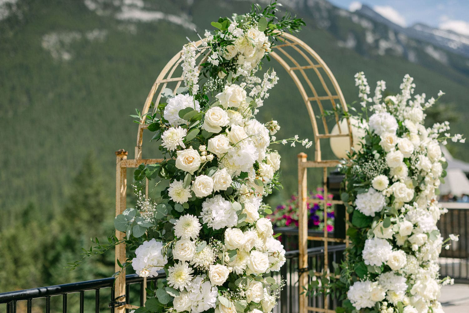 A beautifully arranged wedding arch featuring lush white flowers and greenery, set against a mountainous backdrop.