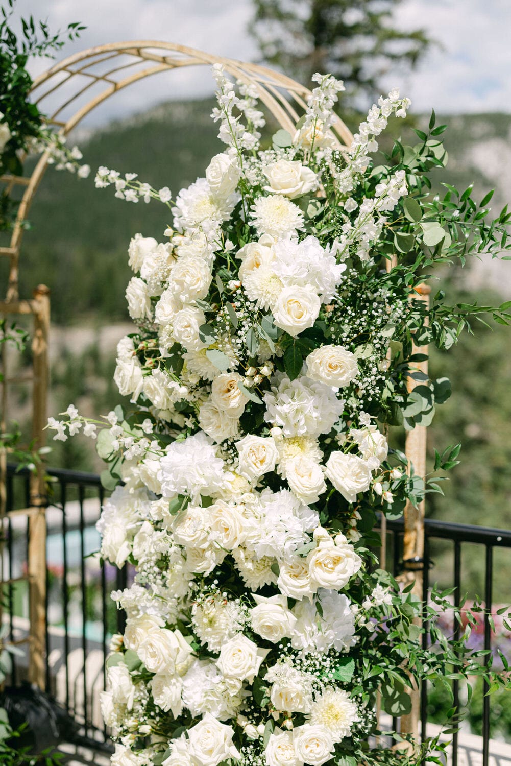 A stunning display of white roses, dahlias, and delicate greenery, set against a backdrop of lush nature, perfect for a wedding ceremony.