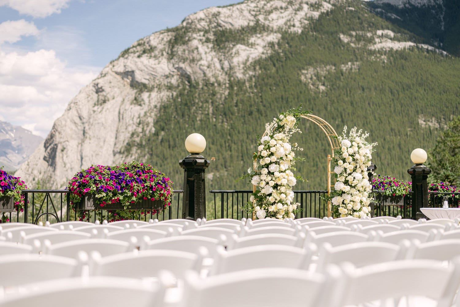 An elegant outdoor wedding venue featuring white chairs, floral arrangements, and a picturesque mountain backdrop.