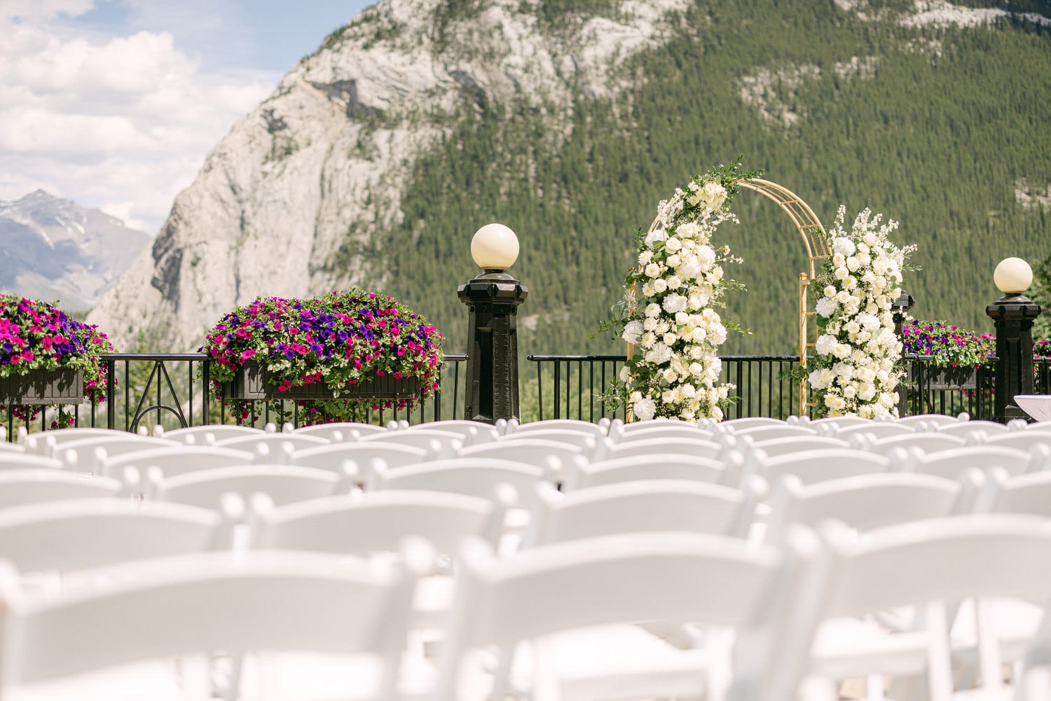 Elegant outdoor wedding ceremony setup with white chairs, floral arrangements, and a scenic mountain backdrop.