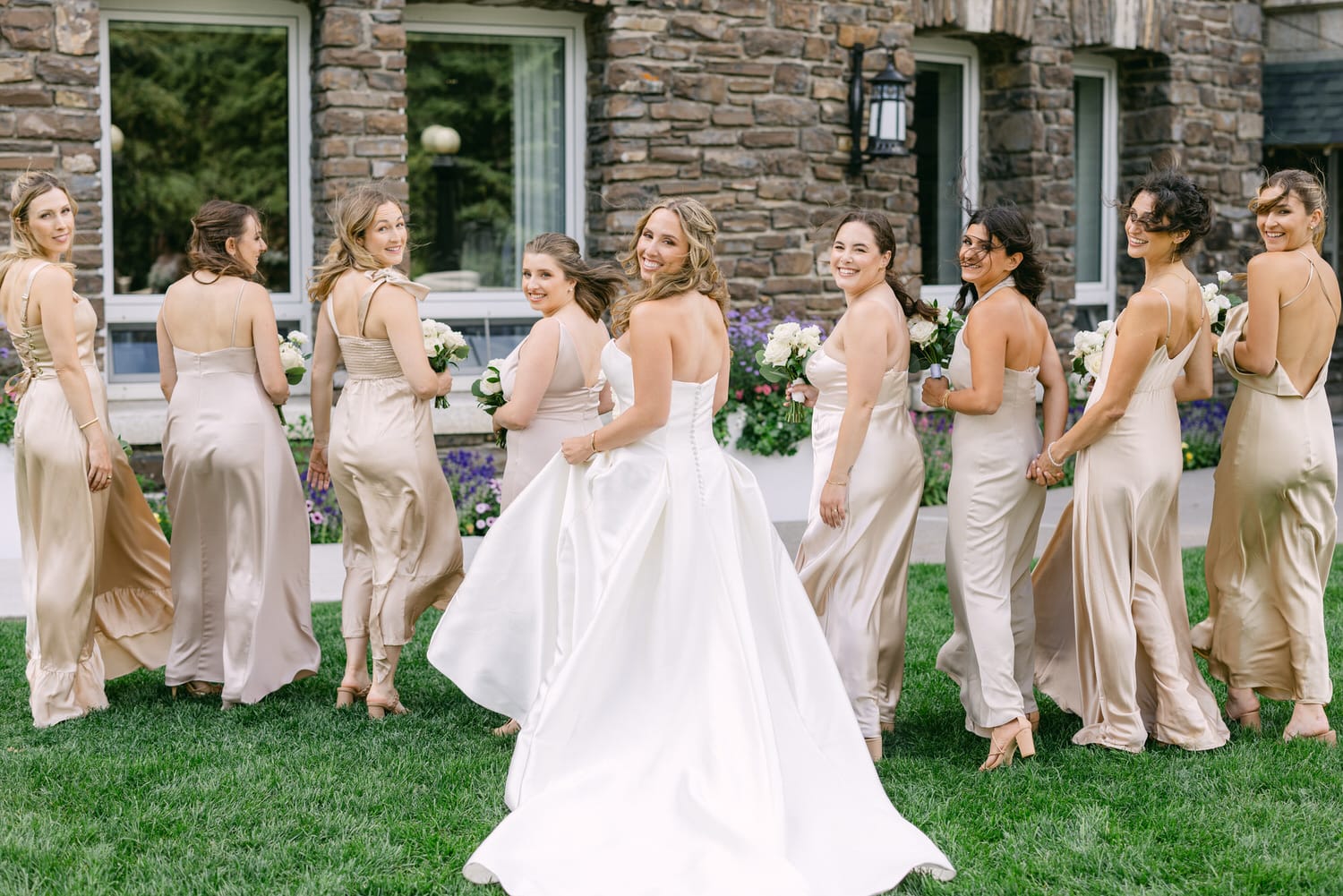 Bridal Party Joy::A bride and her bridesmaids in elegant satin dresses pose outdoors, showcasing their smiles and floral bouquets against a picturesque backdrop.