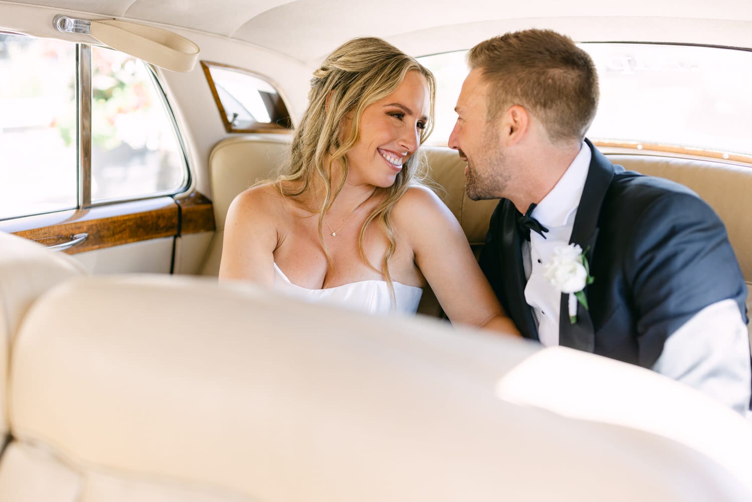 A happy newlywed couple sharing a loving glance inside a vintage car, showcasing their affection on a special day.