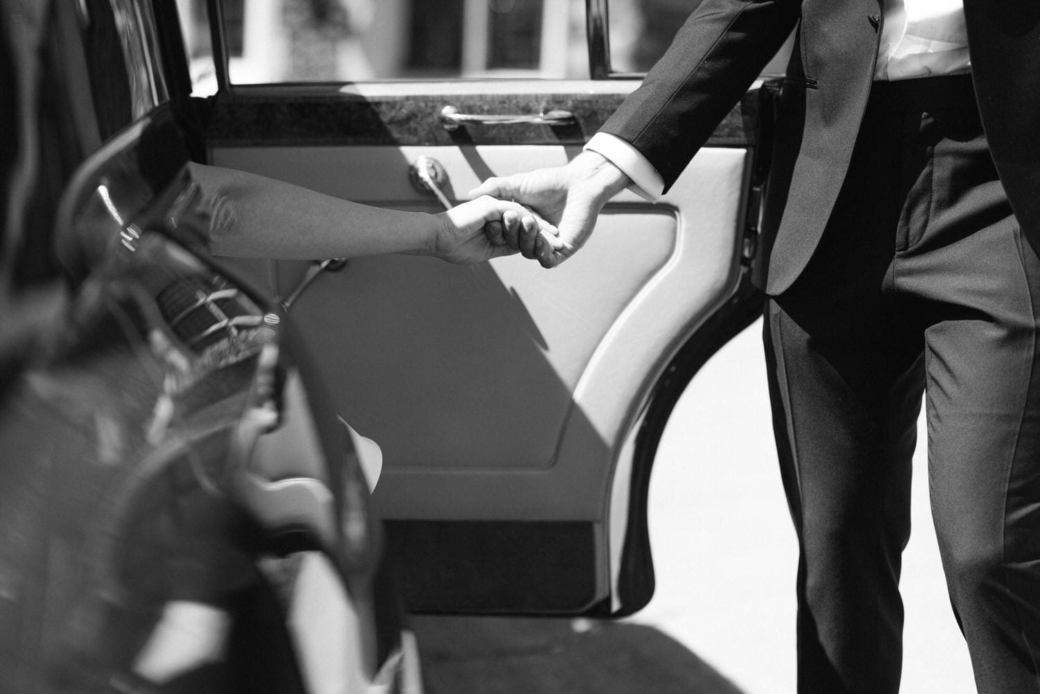 A close-up black and white image capturing two hands, one reaching out from a car, as they clasp together in a gesture of help.