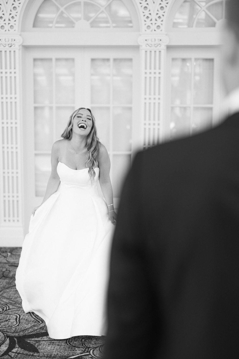 A laughing bride in a white wedding dress captures a moment of happiness, posed in front of an ornate background.