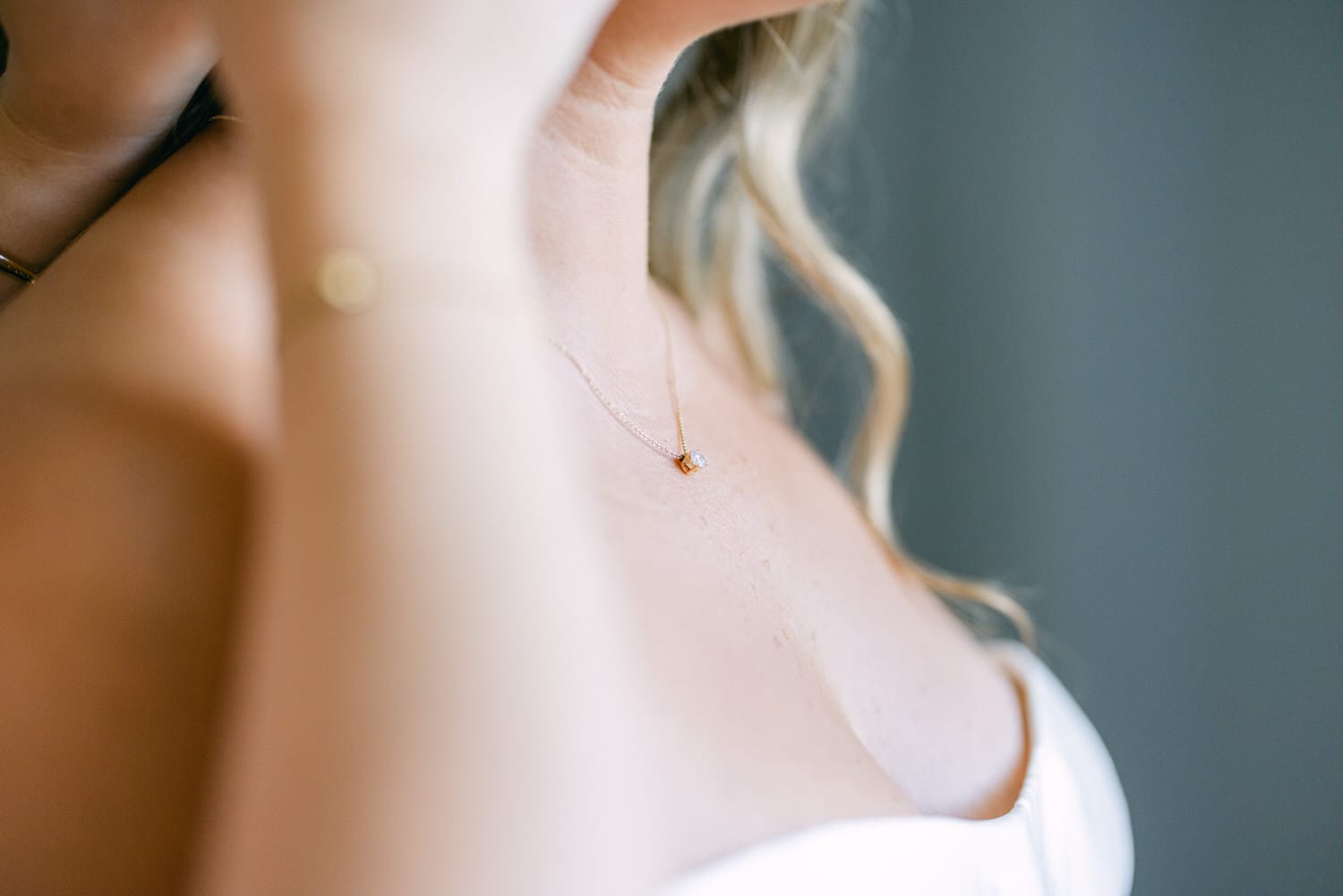 Close-up of a woman adjusting her delicate gold necklace, showcasing the intricate design and her elegant neckline.