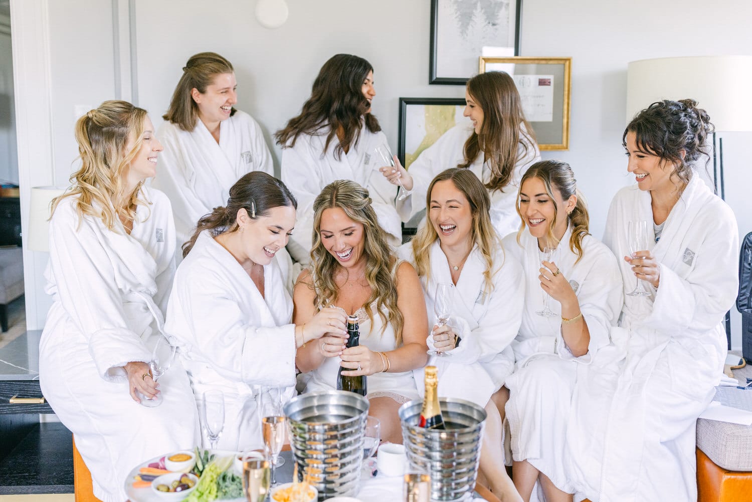 A joyful group of bridesmaids in white robes enjoying a celebratory moment while preparing champagne.