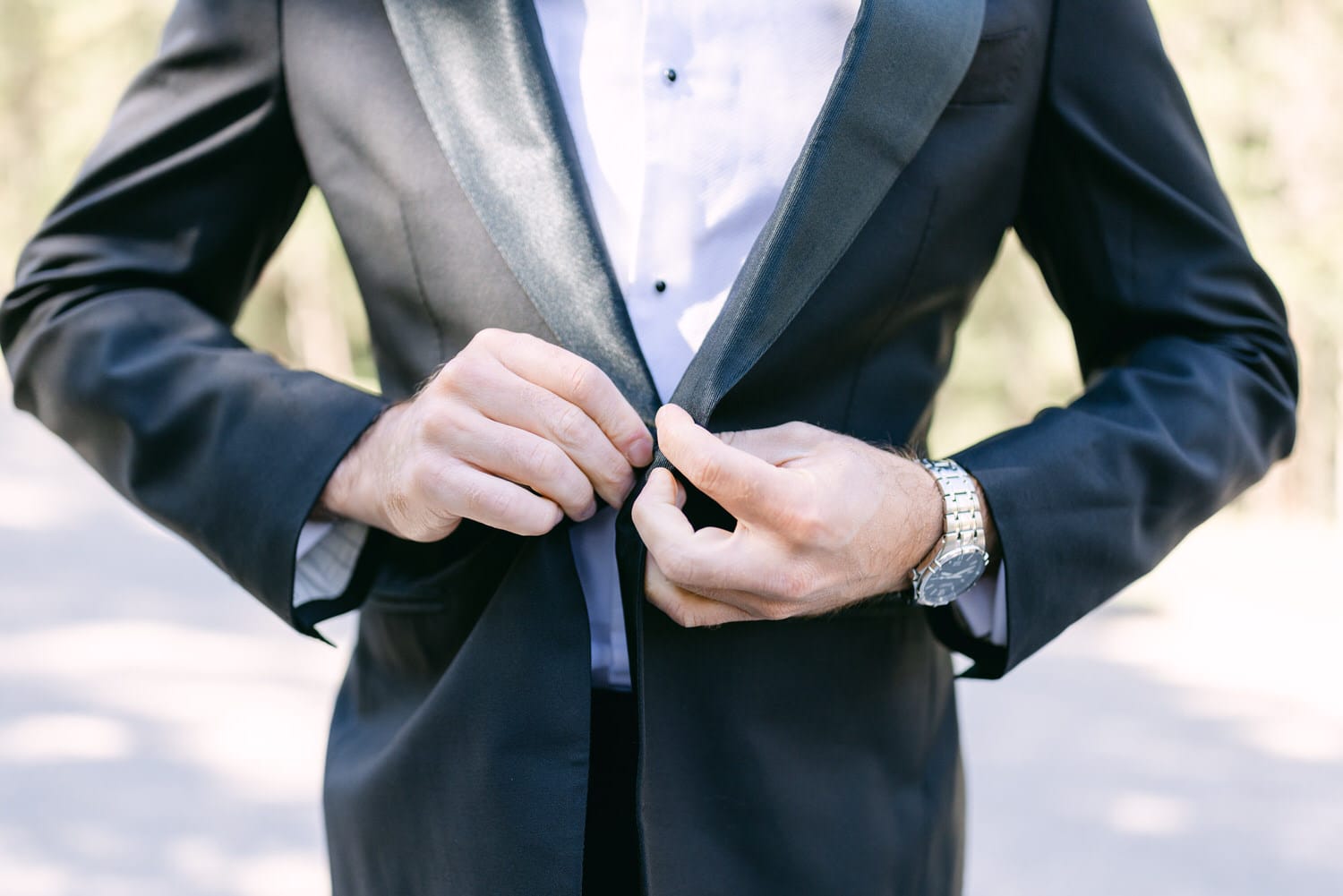 A close-up of a man adjusting the buttons on his tuxedo jacket, showcasing his stylish attire and watch.