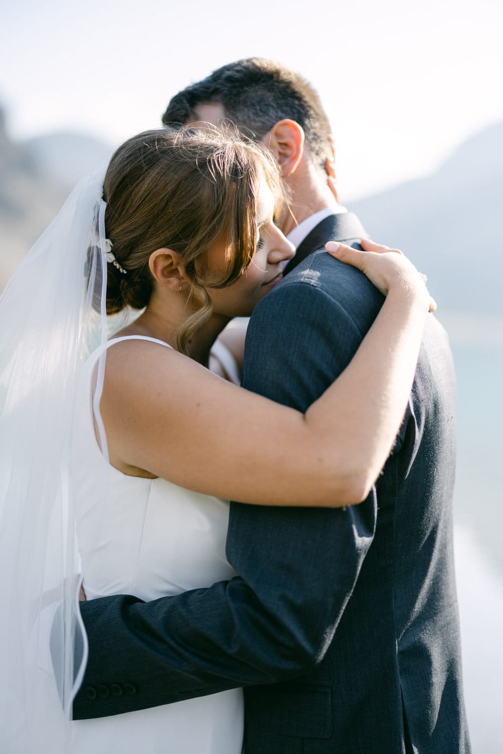 A bride lovingly embraces her groom, capturing a tender moment in a scenic outdoor setting.