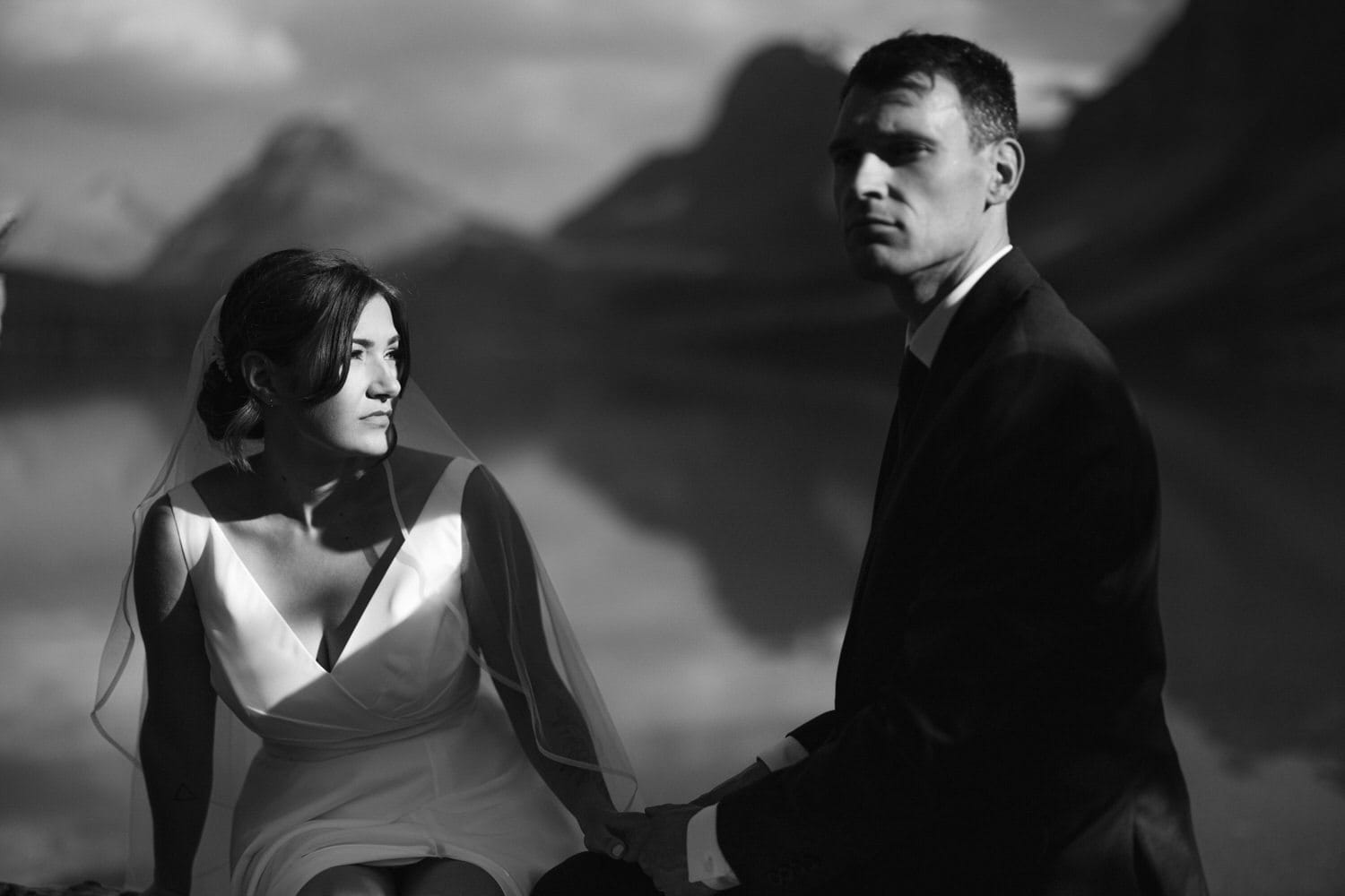 A bride and groom sitting by a serene lake, bathed in soft light, showcasing an intimate moment during their wedding photoshoot.