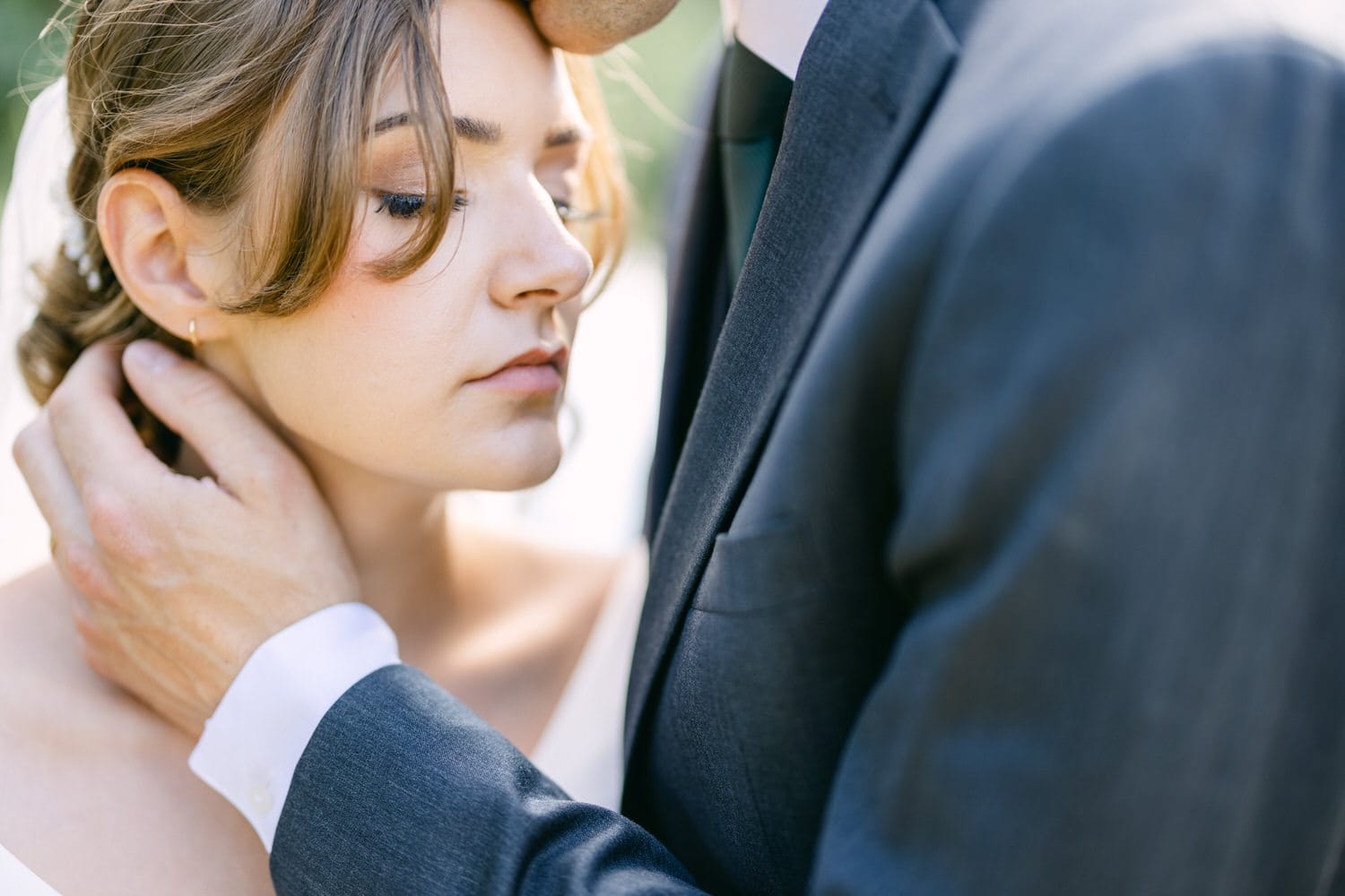 Close-up of a couple embracing, highlighting the bride's serene expression and the groom's tender gesture.