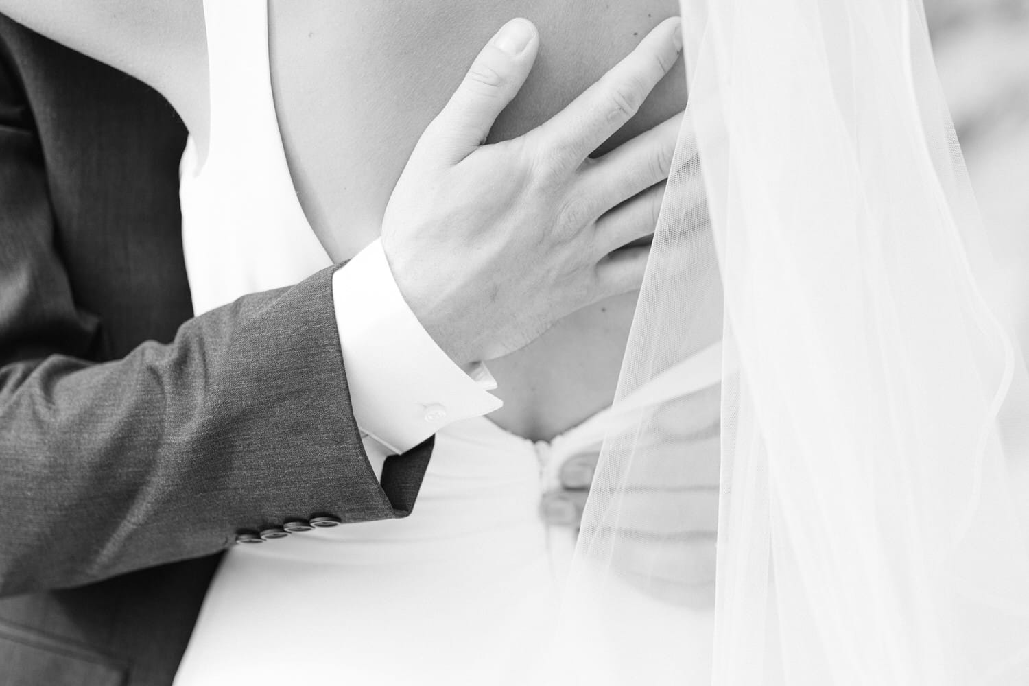 A close-up of a couple's hands, showcasing a gentle embrace with a wedding dress and veil.