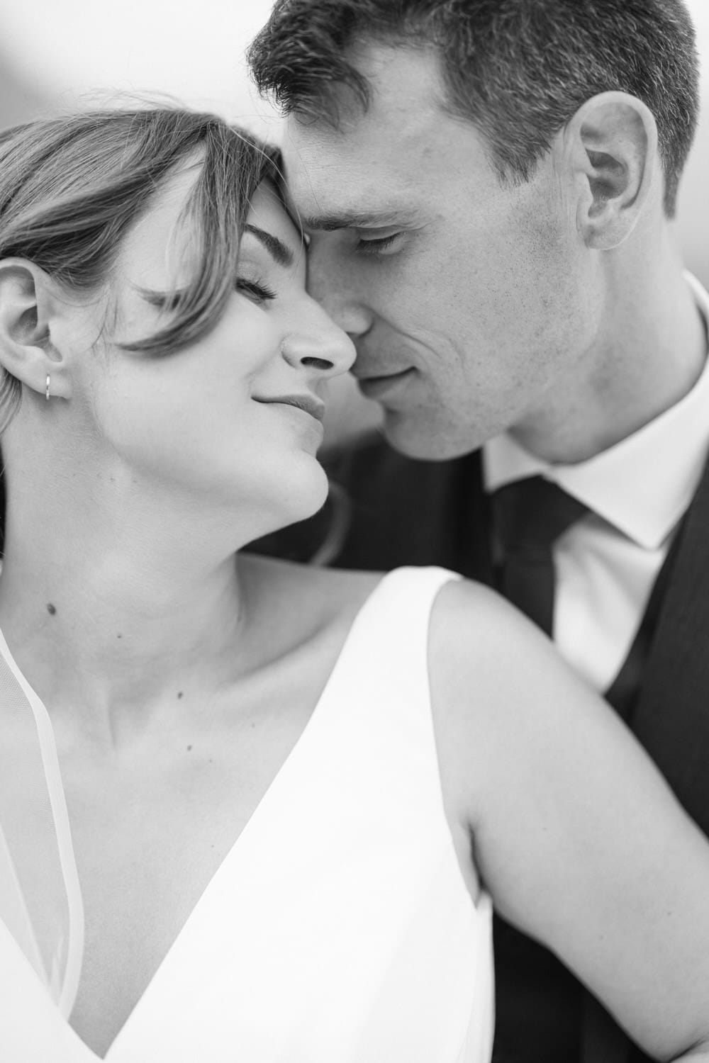 A black and white close-up of a bride and groom sharing a tender moment, their foreheads touching and eyes closed, exuding intimacy and affection.