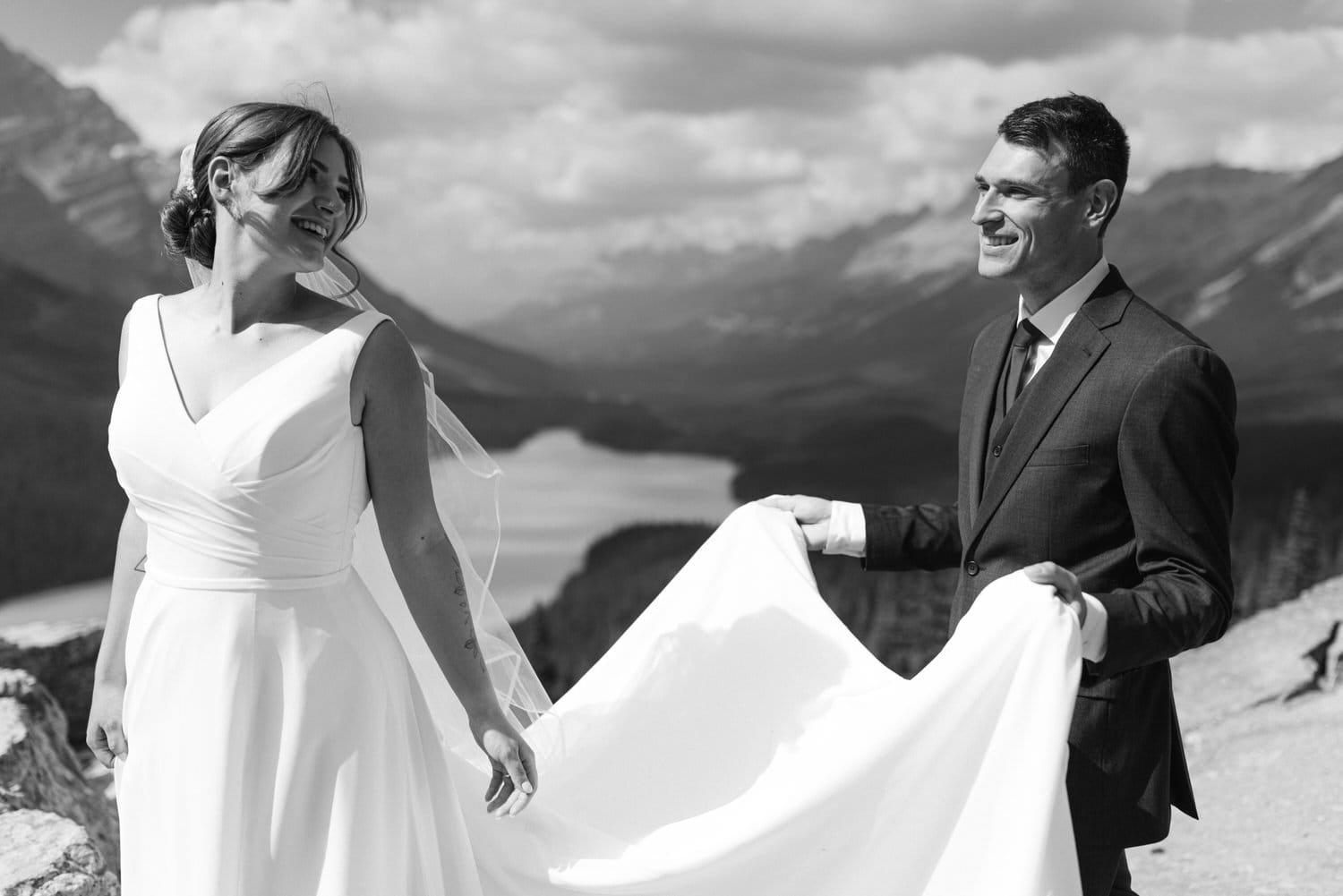 Couple enjoying their wedding day against a stunning mountain backdrop, with the bride playfully holding her dress.