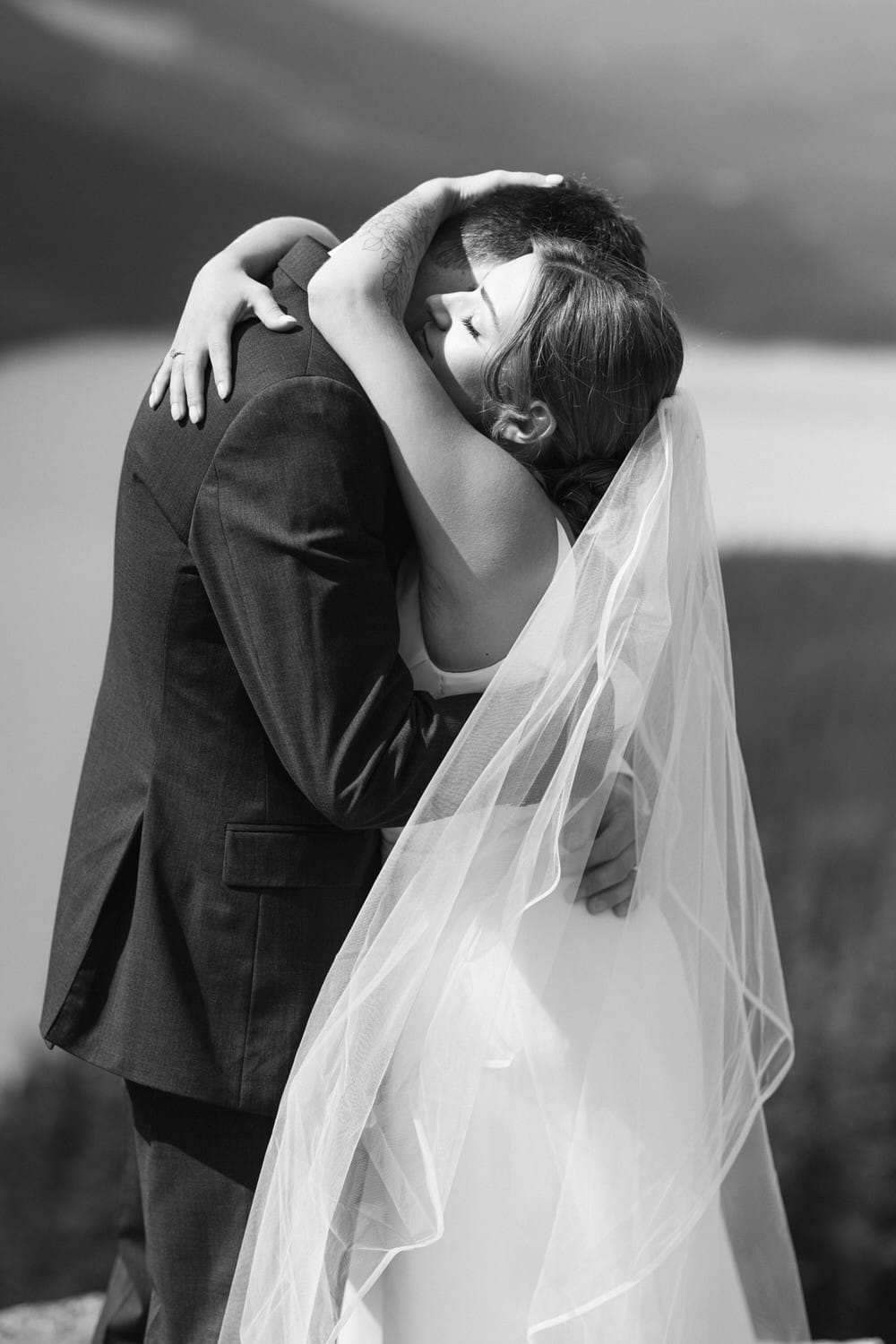 A close-up of a bride and groom embracing passionately, with the bride's veil flowing gently in the breeze.