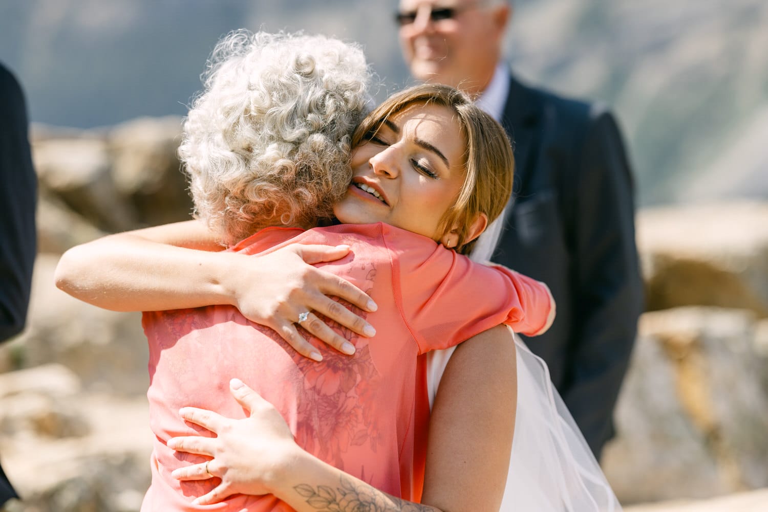 A bride hugs her grandmother warmly during a wedding ceremony, capturing a heartfelt moment filled with love and joy.