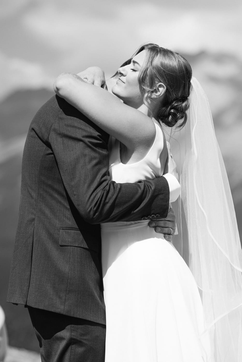 A bride embracing her groom, showcasing a moment of joy and love during their wedding ceremony in a scenic outdoor setting.