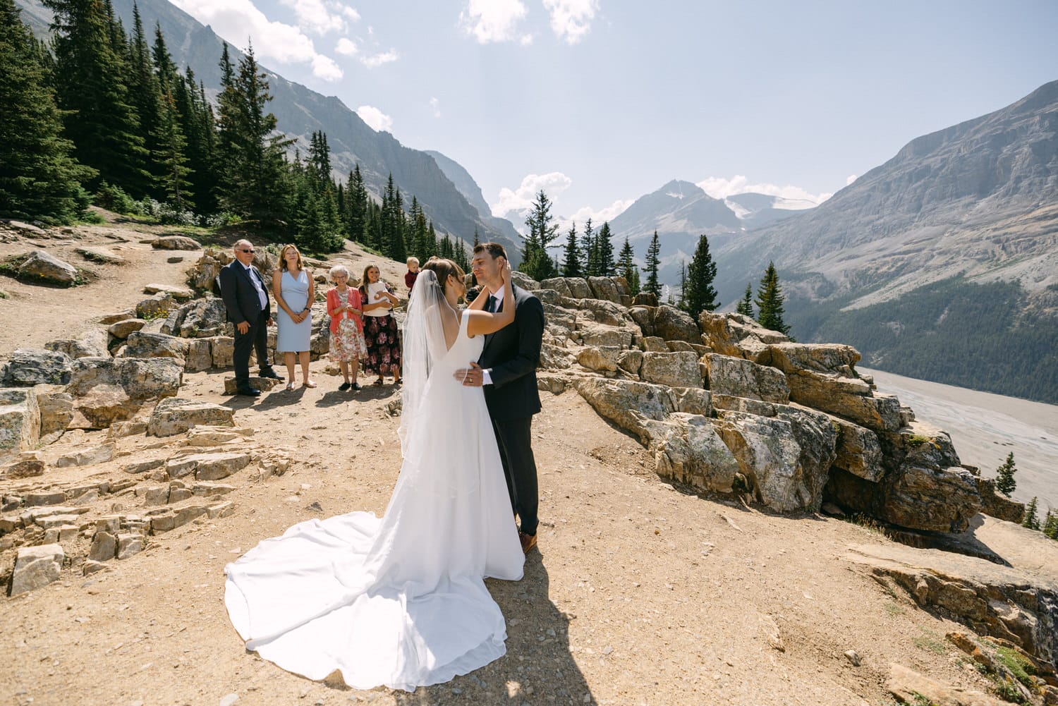 A couple exchanges vows during an outdoor wedding ceremony surrounded by stunning mountain scenery and guests.