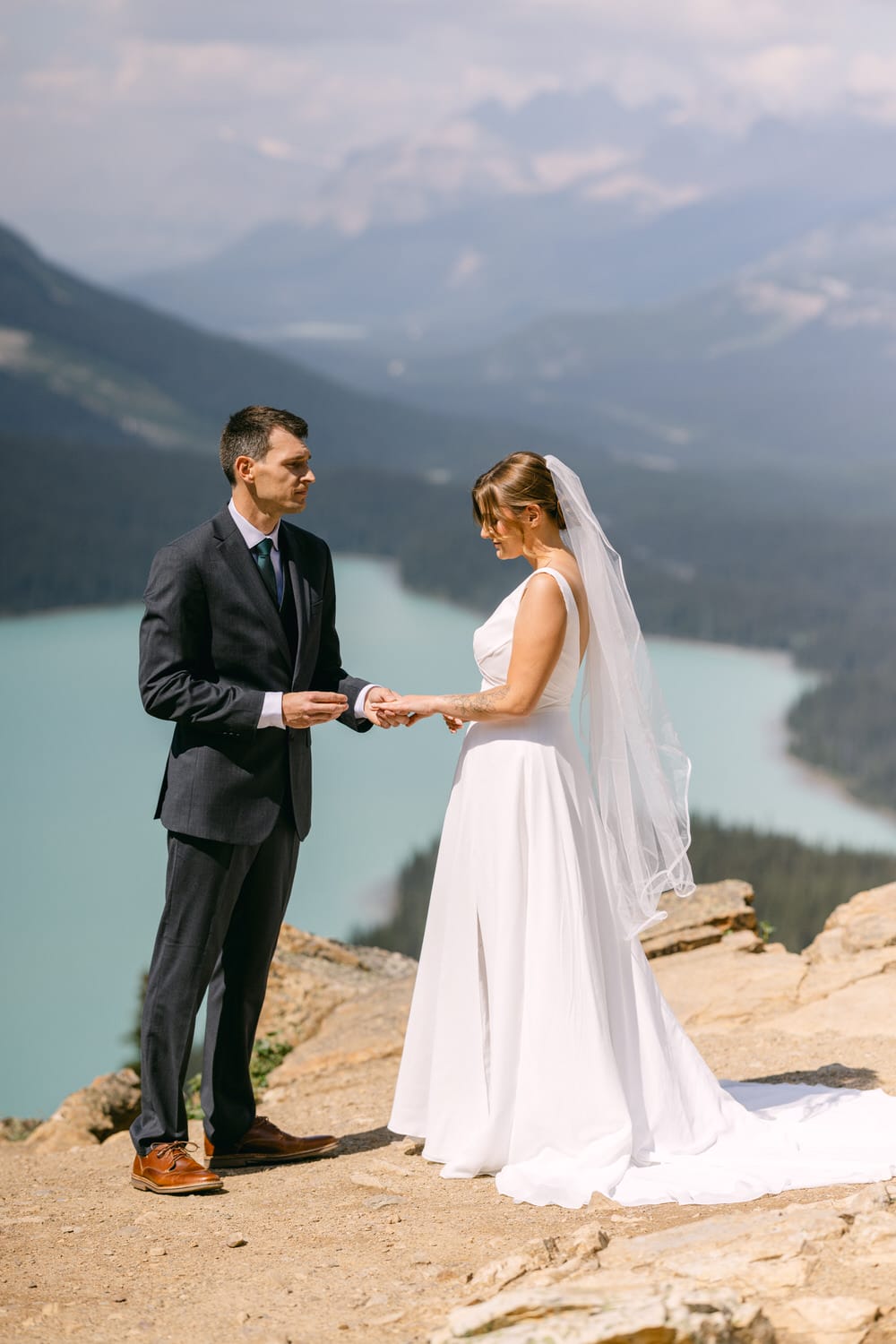 A couple exchanges vows during their outdoor wedding, with a stunning mountain landscape and turquoise lake in the background.