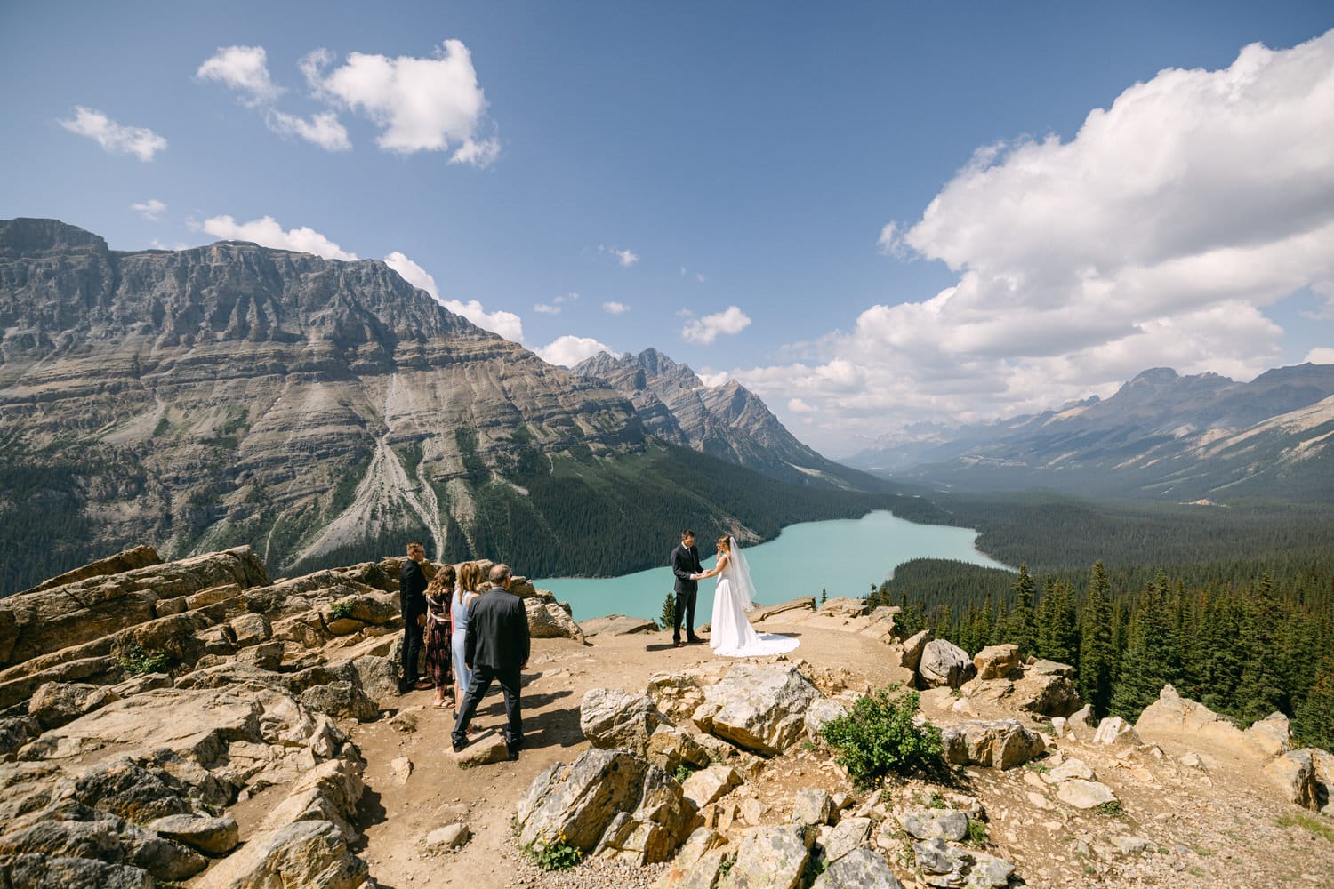 A couple exchanging vows at a picturesque outdoor wedding ceremony surrounded by mountains and a turquoise lake.