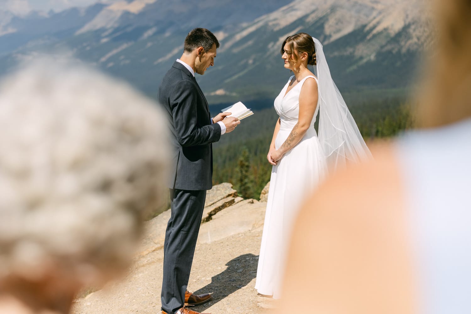 A bride and groom exchange vows during an outdoor wedding ceremony with mountains in the background, capturing a moment of love and commitment.