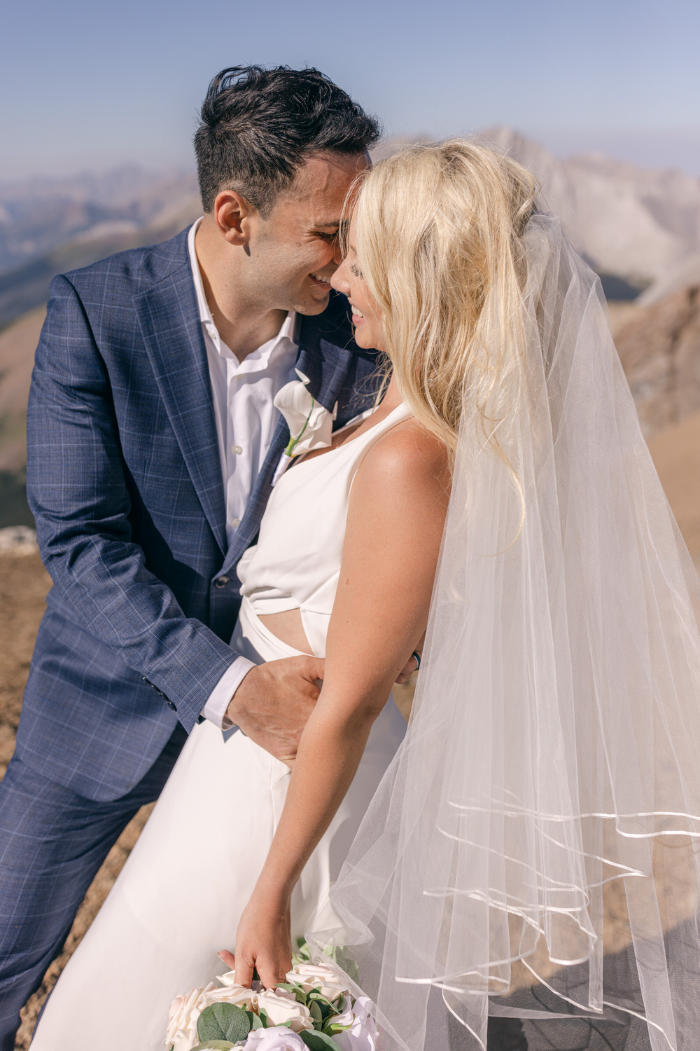 A joyful couple sharing an intimate moment while embracing, surrounded by scenic mountain views on their wedding day.