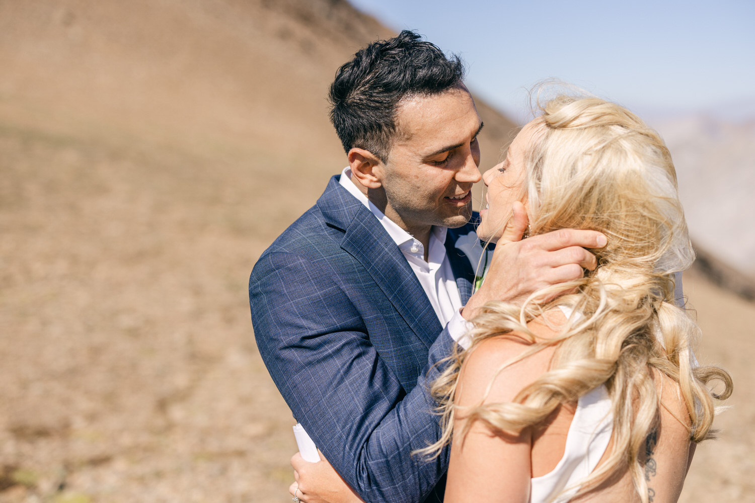 A couple sharing a tender moment in a scenic outdoor setting, with the man gently holding the woman's face as they lean in for a kiss.