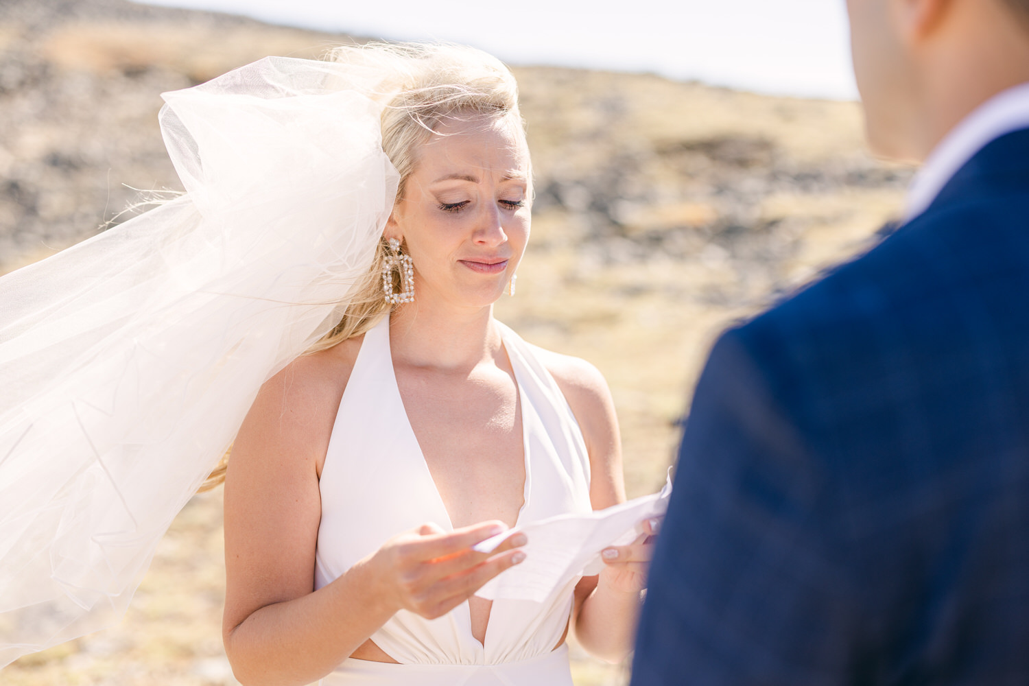 A bride reading heartfelt vows outdoors, with her veil gently blowing in the wind.