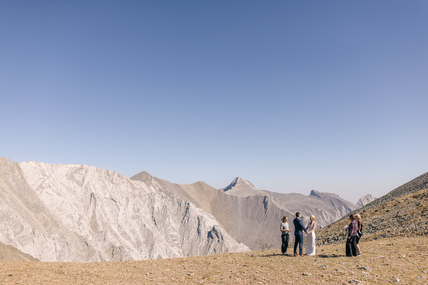 A couple exchanges vows amidst stunning mountain scenery, surrounded by friends and family in a serene outdoor setting.