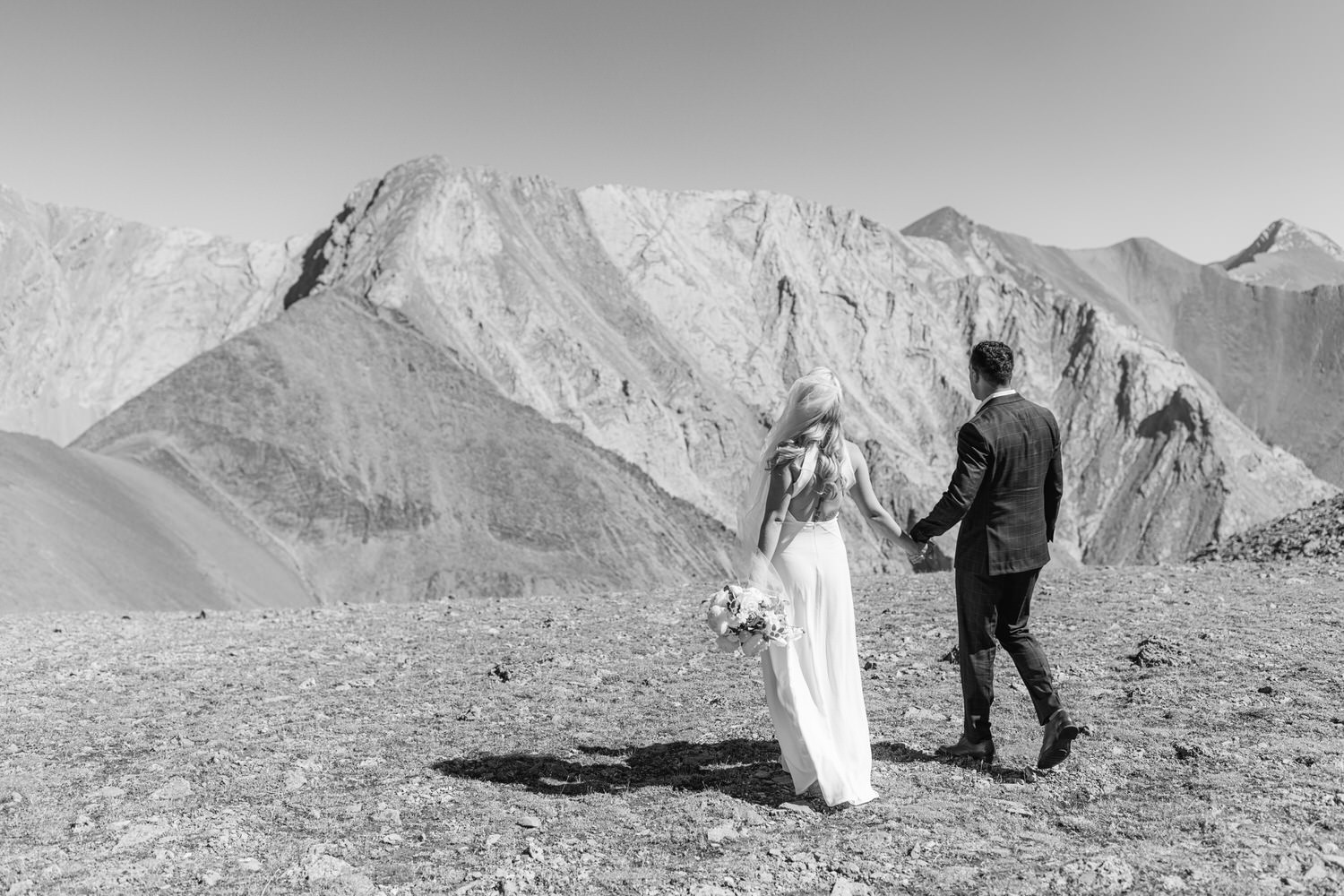 A couple holding hands, walking towards a breathtaking mountainous landscape, capturing a moment of love and adventure.