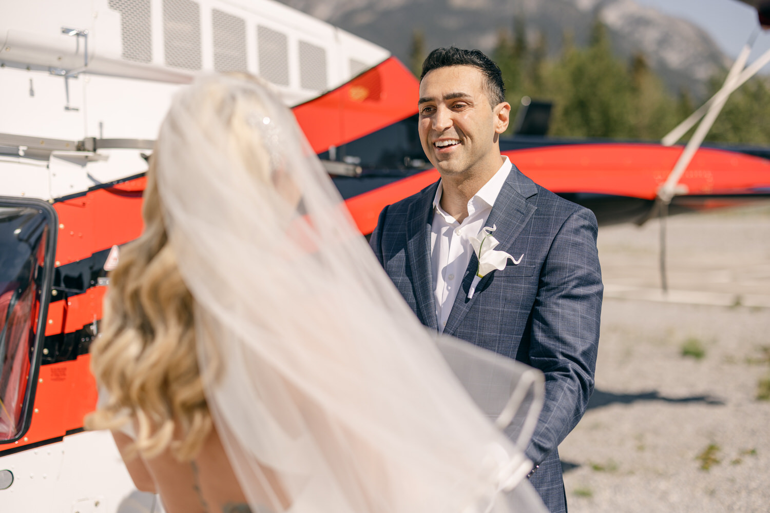 A smiling groom stands before his bride, with a helicopter in the background, capturing a moment of love and joy on their special day.