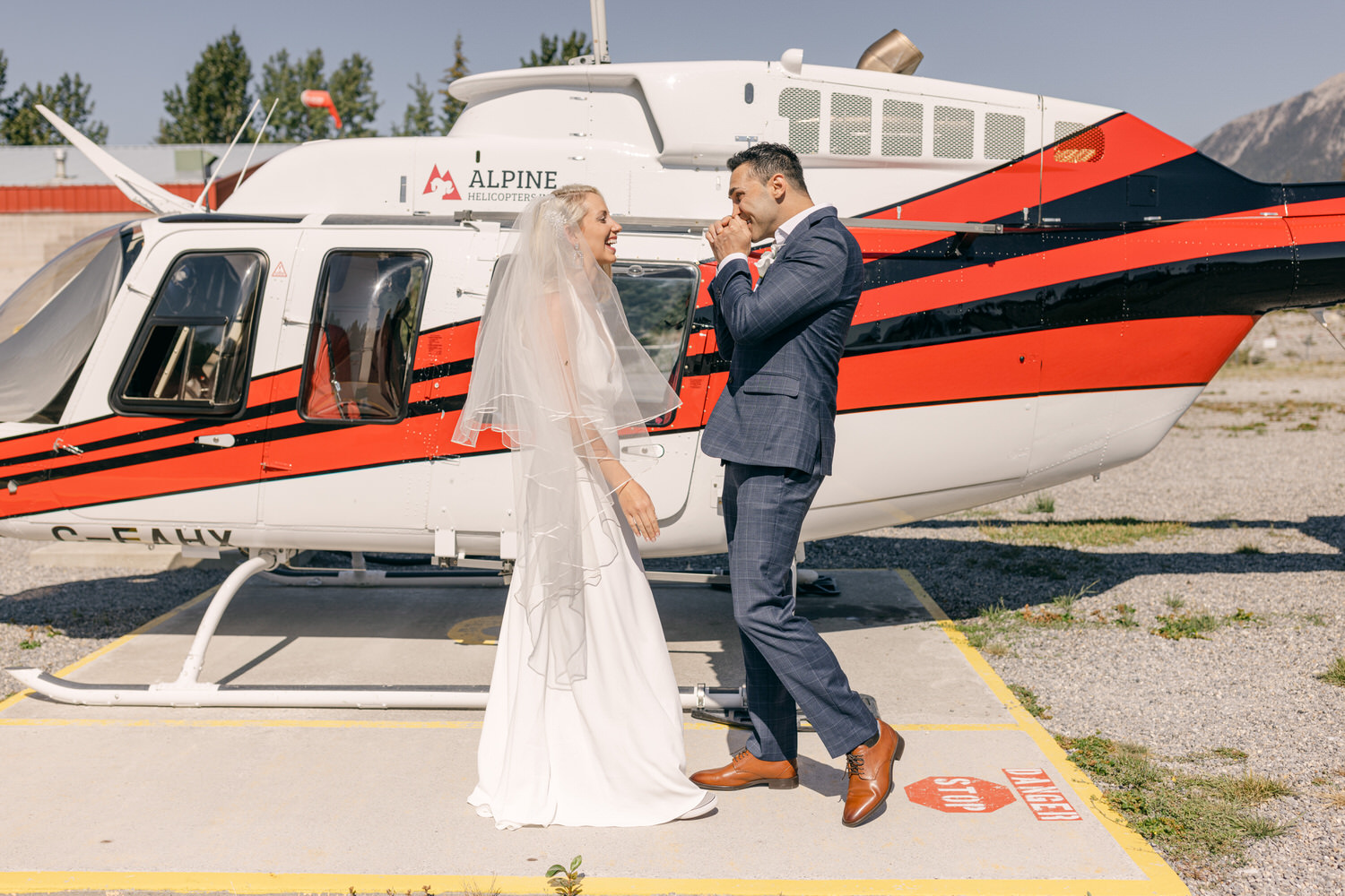 A joyful couple shares a moment together in front of a red and white helicopter, celebrating their wedding day.