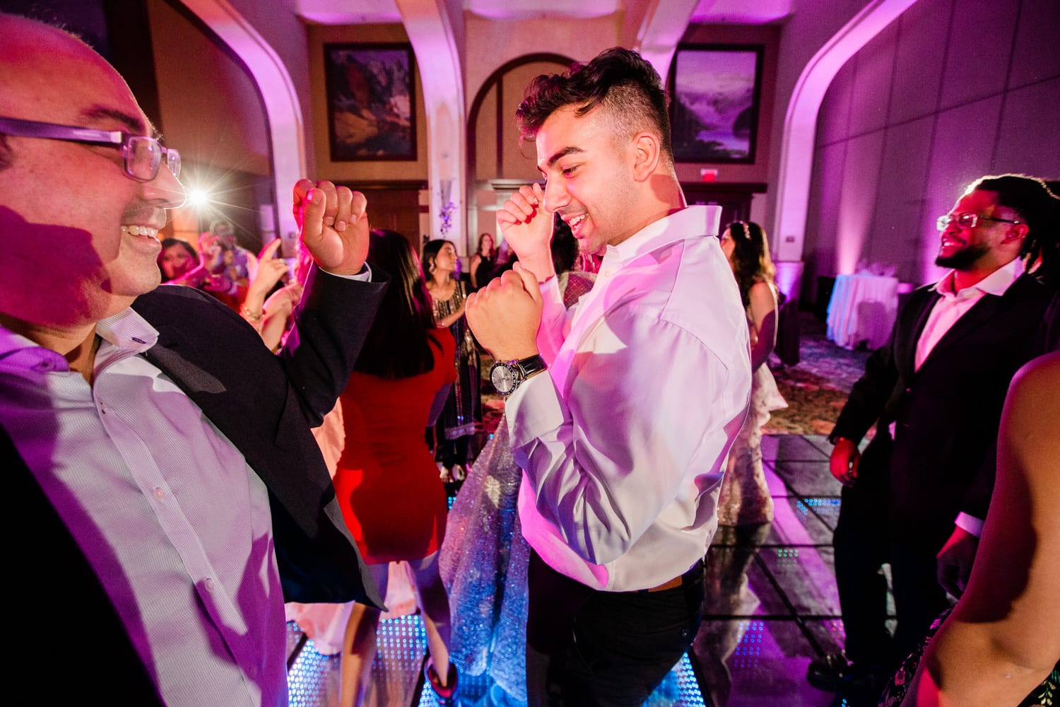 Guests dancing joyfully at a lively event with vibrant lighting and a festive atmosphere.