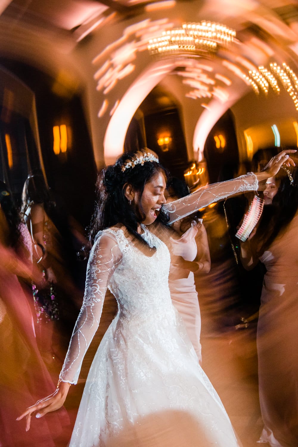 A joyful bride in a sparkling wedding dress dances with excitement, surrounded by friends in a lively, illuminated atmosphere.