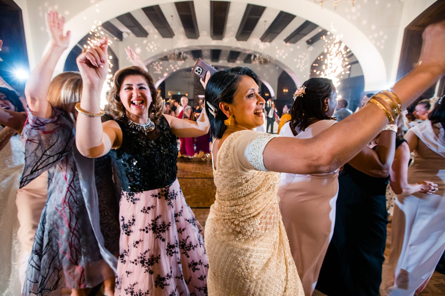 Women dancing joyfully at an elegant event, illuminated by sparklers in a festive atmosphere.