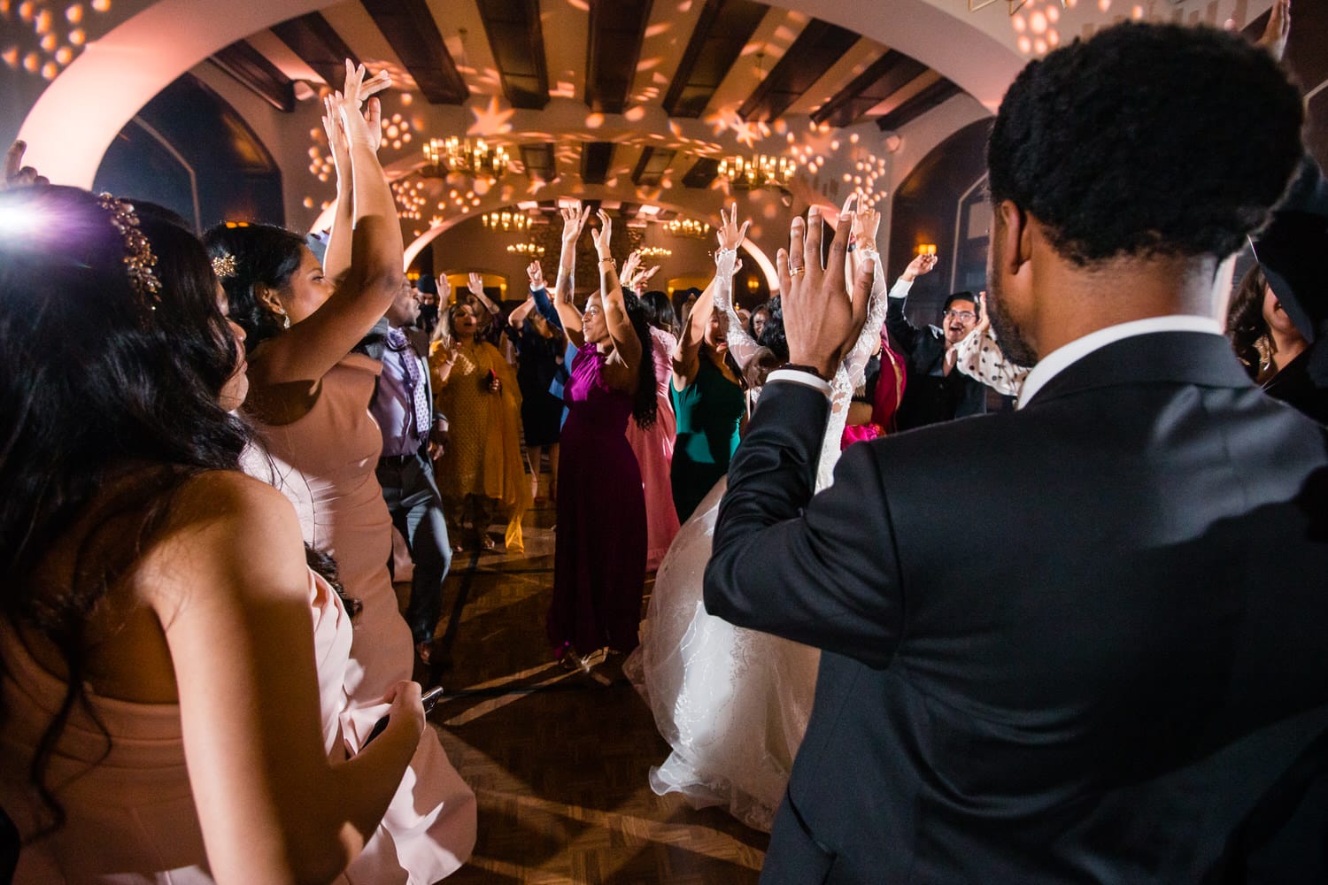 Guests joyfully dancing with hands raised, illuminated by festive lights at a lively event.