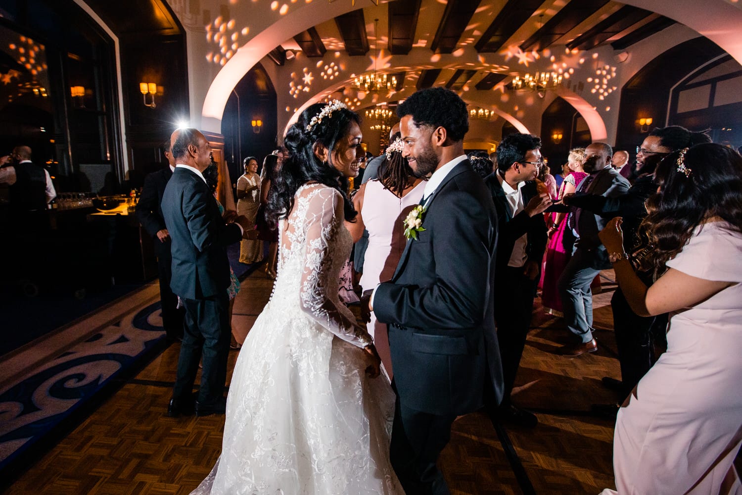 A couple shares a romantic moment on the dance floor during a lively wedding celebration, surrounded by guests and twinkling lights.