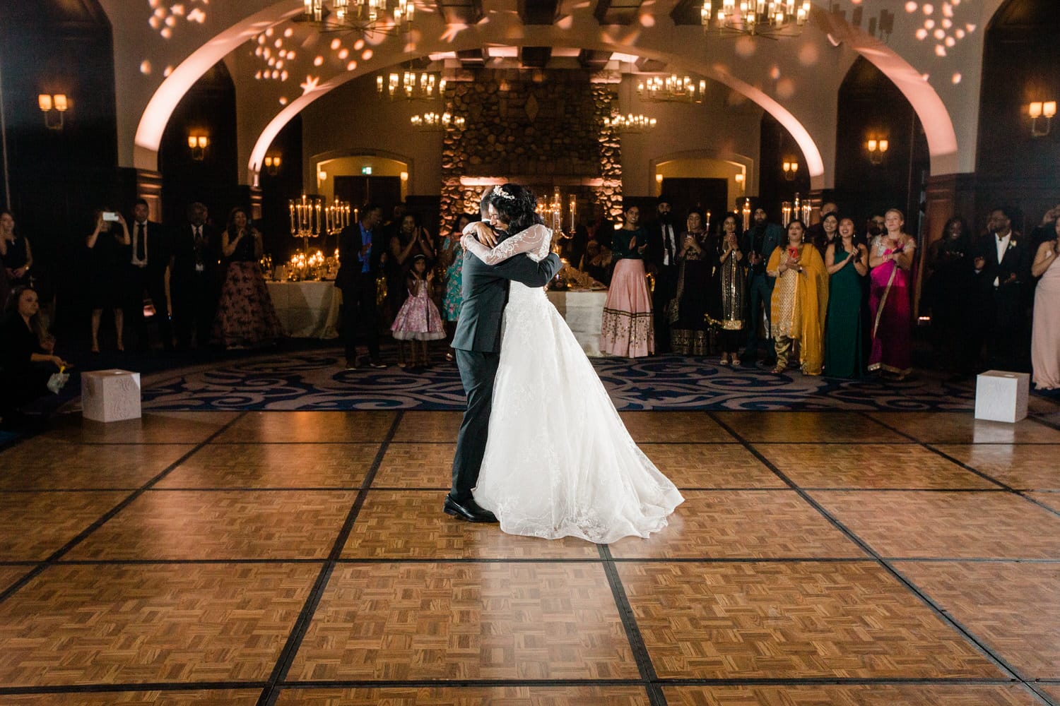 A couple in formal attire shares an intimate moment while dancing at their wedding reception, surrounded by guests watching in celebration.