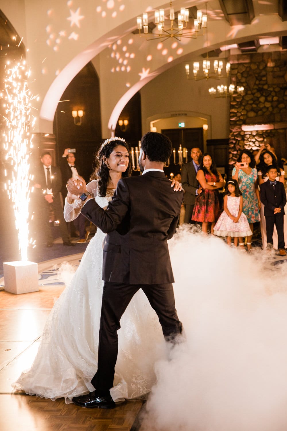 A couple shares a romantic first dance amid bright lights and guests, creating a joyful atmosphere at their wedding reception.