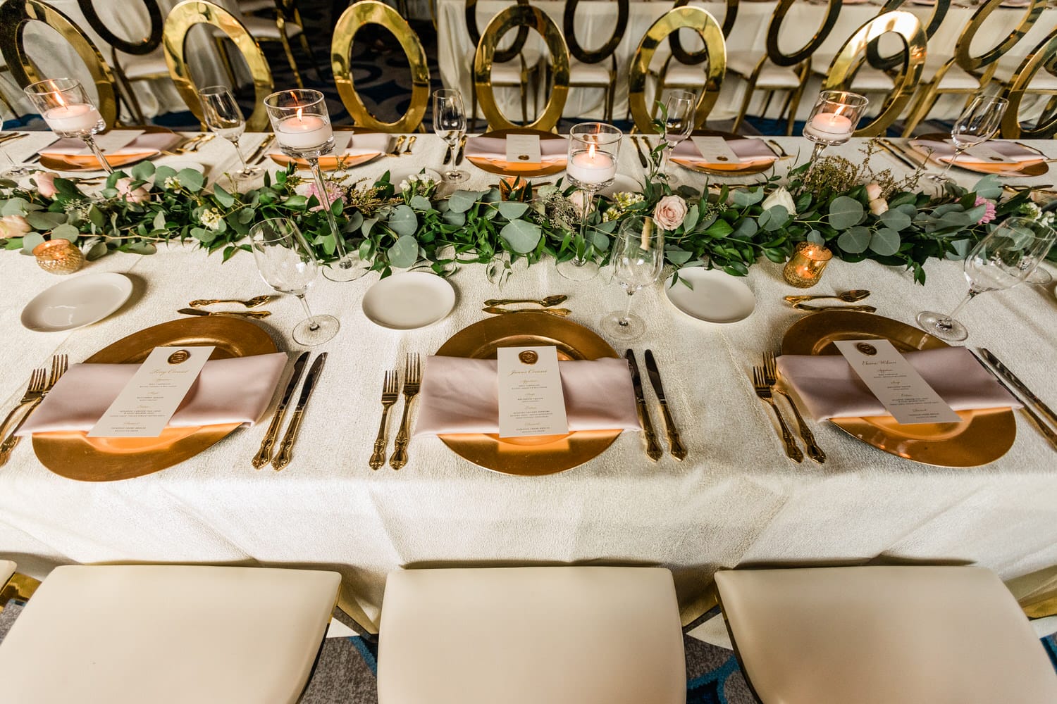 A beautifully arranged table featuring gold chargers, pink napkins, and a floral centerpiece, creating an inviting atmosphere for a special occasion.