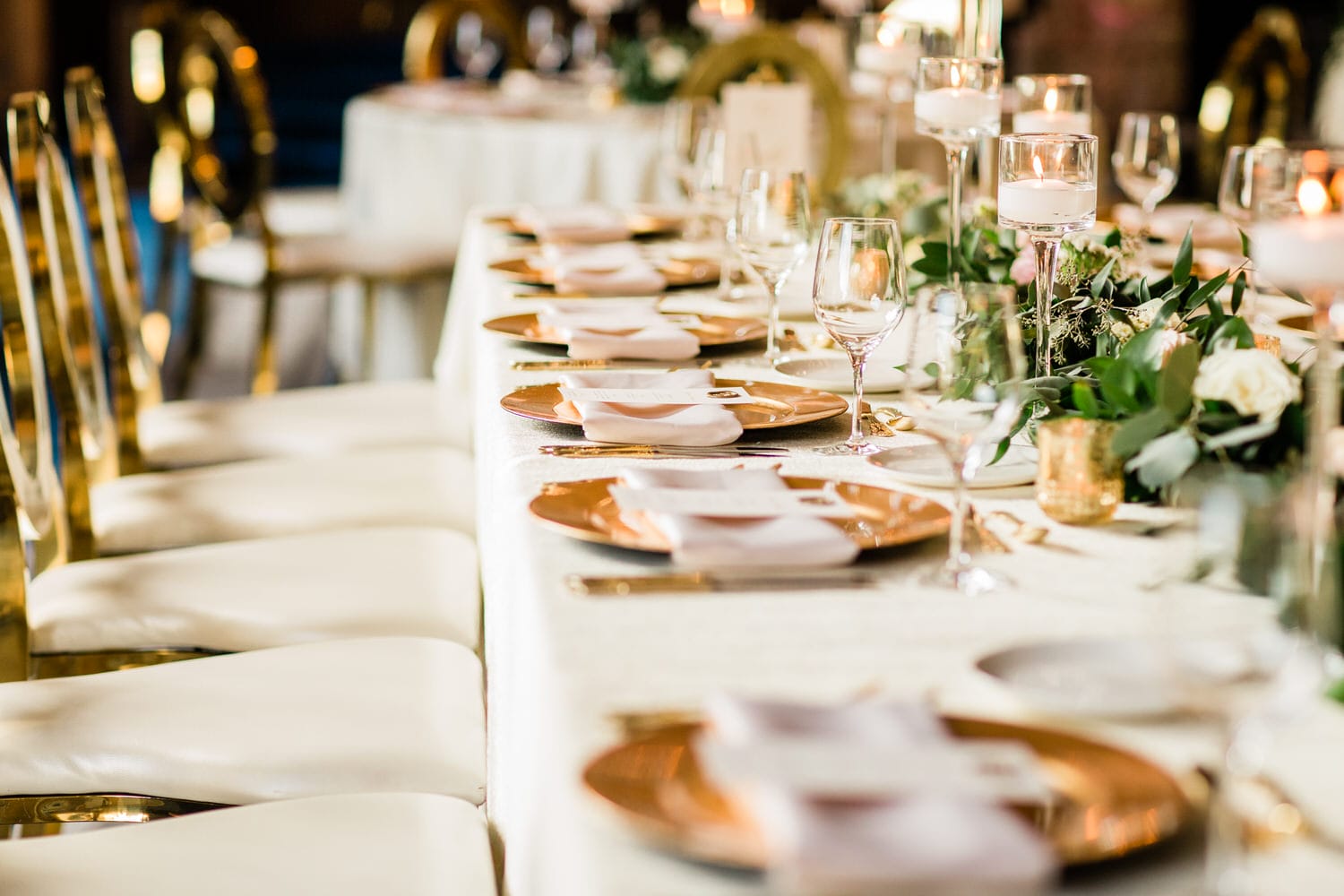 A beautifully arranged dining table featuring gold plates, glassware, and floral centerpieces, ready for a formal event.