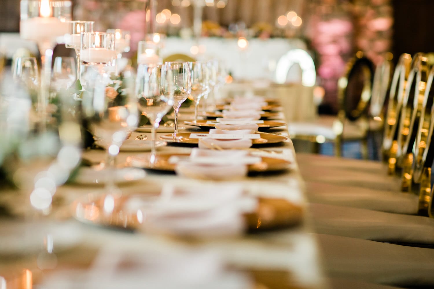 A beautifully arranged dining table with glassware, gold plates, and candles, set for a special event.