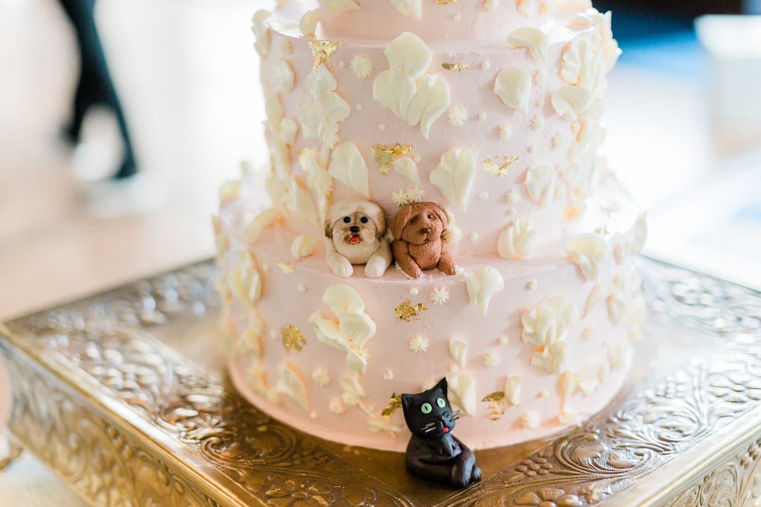 A beautifully crafted pink cake adorned with edible dog figurines and floral decorations, set on an ornate golden stand.