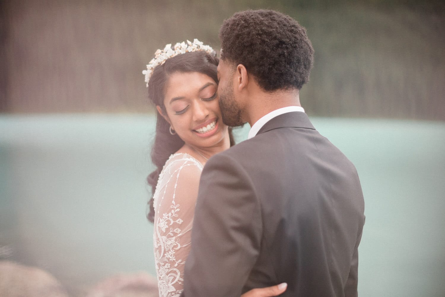 A bride and groom share a tender moment by a serene lakeside, surrounded by nature's beauty.