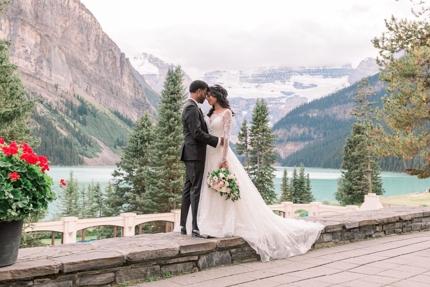 A couple embraces in a romantic moment surrounded by stunning mountains and lush greenery, with a calm lake in the background.