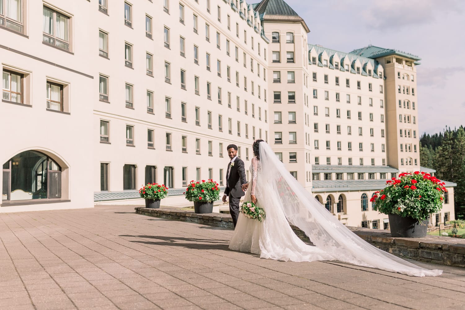 A bride and groom walking hand in hand outside a beautiful hotel, adorned with flowers and surrounded by lush greenery.