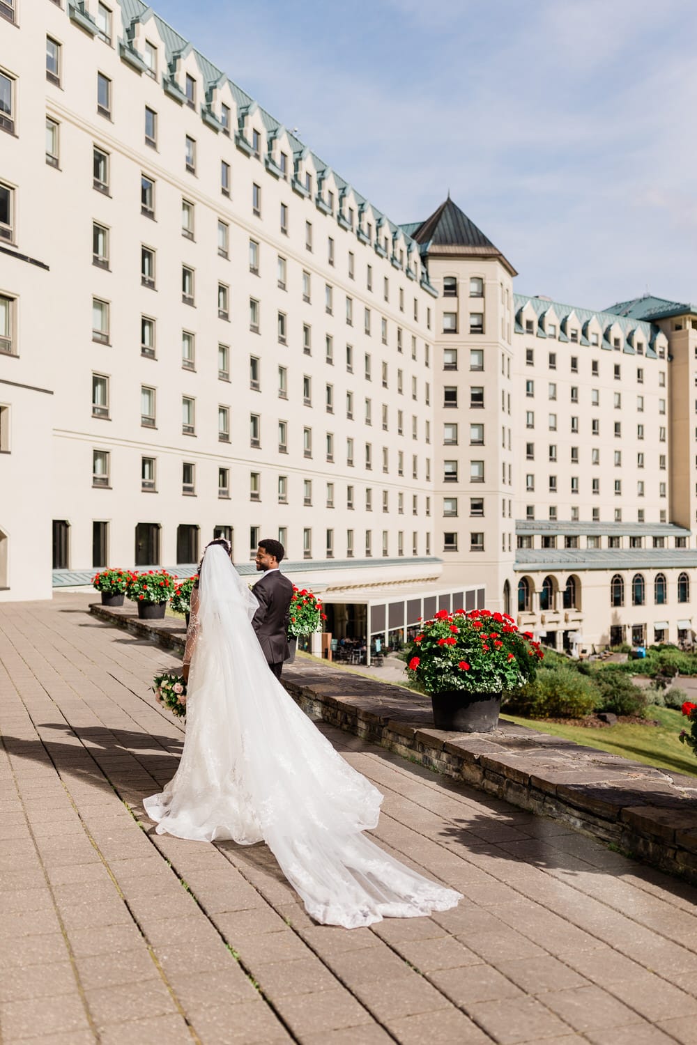 A couple holding hands and walking away from the grand hotel with vibrant flower planters in the foreground.