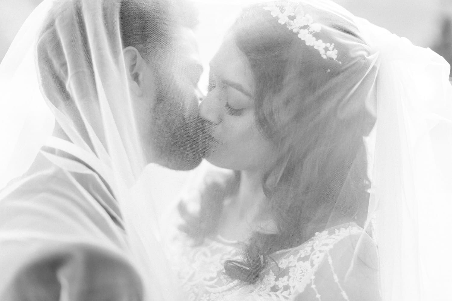 A loving couple sharing a kiss under a veil, capturing a moment of intimacy and celebration on their wedding day.