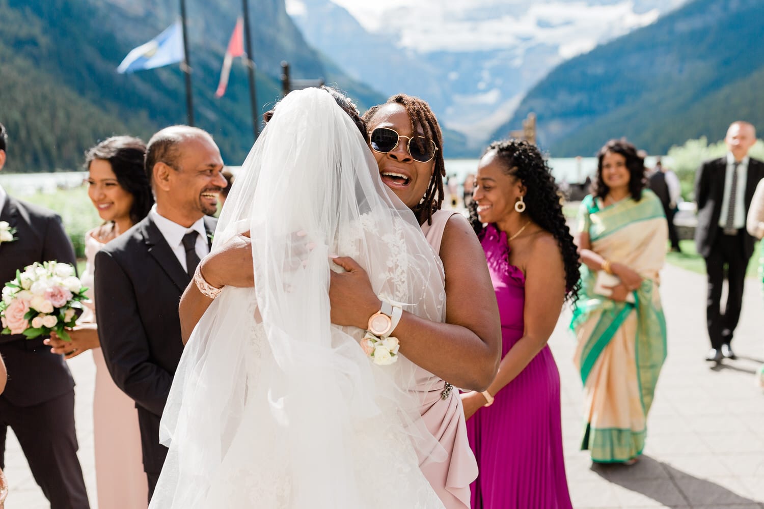 A joyful moment as the bride hugs a friend in a picturesque outdoor wedding setting surrounded by mountains.