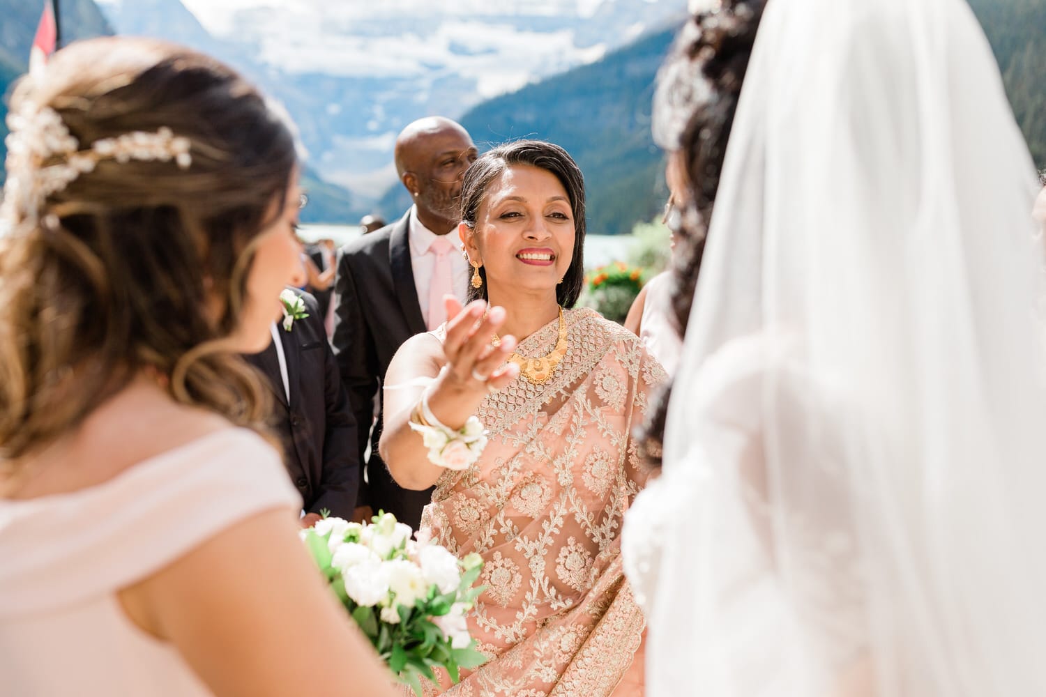 Wedding Celebration in Nature::A joyful moment at a wedding ceremony with a woman in traditional attire greeting guests against a stunning mountain backdrop.