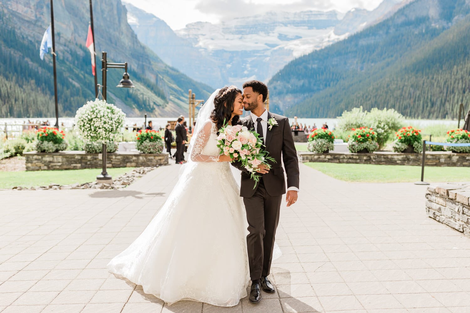 A joyful couple embraces amidst the stunning backdrop of Lake Louise, surrounded by flowers and mountains, on their wedding day.